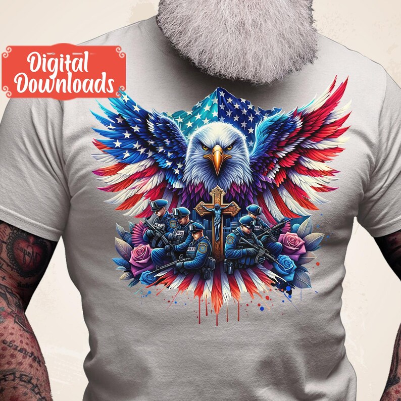 May include: A gray t-shirt with a graphic of a bald eagle with its wings spread wide, holding a cross. The eagle is superimposed on an American flag. Five police officers are standing in front of the eagle, holding guns and wearing blue uniforms. The graphic is surrounded by red, white, and blue watercolor splatters.