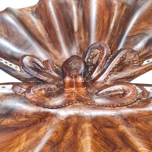 Puede incluir: Una escultura de madera de un pulpo en una concha. El pulpo está tallado en detalle y la concha es de color marrón natural.