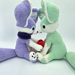 Pu&ograve; includere: Due peluche a forma di volpe all'uncinetto, uno lavanda e l'altro verde menta, con dettagli bianchi. La volpe lavanda indossa una sciarpa viola scuro. Tengono un piccolo cuore rosso. I peluche hanno grandi orecchie e occhi neri.