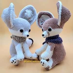 Pu&ograve; includere: Due peluche di volpe Fennec fatti a mano all'uncinetto. Una volpe &egrave; grigio chiaro e bianca, l'altra marrone e bianca. Entrambi hanno grandi orecchie, occhi neri e piccole sciarpe. I peluche sono seduti uno accanto all'altro.