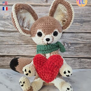 Pu&ograve; includere: Un peluche a forma di volpe fatto a mano all'uncinetto con grandi orecchie, una sciarpa verde e un cuore rosso. La volpe &egrave; principalmente marrone, crema e bianca, con dettagli neri sulle zampe e sulla coda. L'immagine include il testo "PDF ONLY" e bandiere.