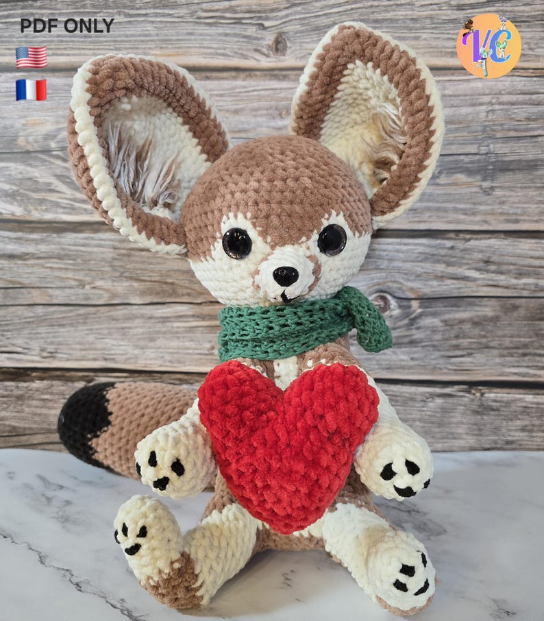 Pu&ograve; includere: Un peluche a forma di volpe fatto a mano all'uncinetto con grandi orecchie, una sciarpa verde e un cuore rosso. La volpe &egrave; principalmente marrone, crema e bianca, con dettagli neri sulle zampe e sulla coda. L'immagine include il testo "PDF ONLY" e bandiere.