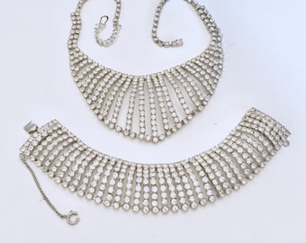 May include: A set of two silver tone rhinestone necklaces. The larger necklace is a choker style with a graduated design. The smaller necklace is a shorter, more delicate style.