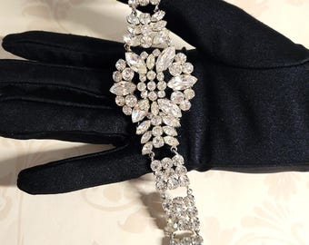 May include: A vintage rhinestone bracelet with a large, ornate, floral-shaped design. The bracelet is made of silver-toned metal and features clear rhinestones of various sizes.