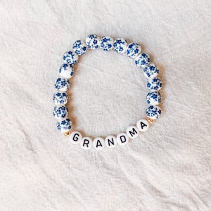 May include: A white and blue floral patterned beaded bracelet with the word "GRANDMA" spelled out in black letters on white beads.