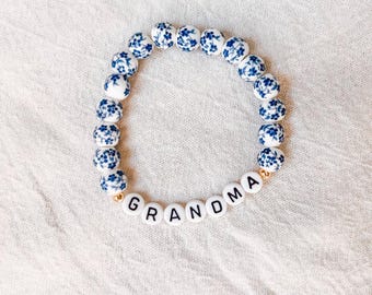 May include: A white and blue floral patterned beaded bracelet with the word "GRANDMA" spelled out in black letters on white beads.