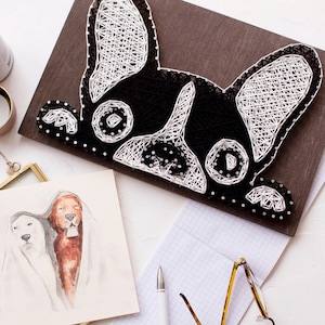 May include: A black and white string art piece depicting a French Bulldog's head. The artwork is mounted on a dark brown wooden board.
