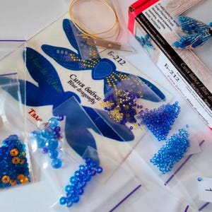 Puede incluir: Un kit de cuentas de lib&eacute;lula azul con fondo blanco, cuentas azules y doradas y una bolsa de pl&aacute;stico transparente con una etiqueta con el n&uacute;mero 1.