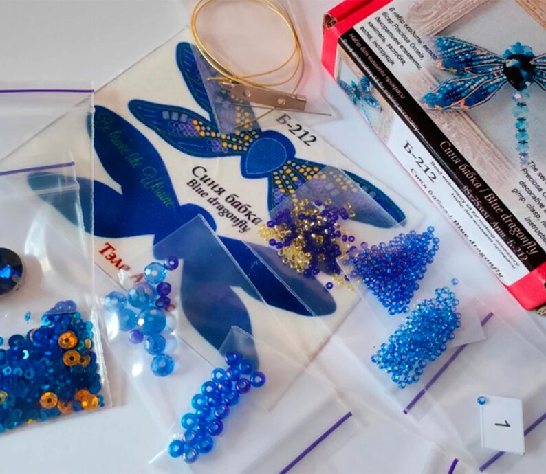 Puede incluir: Un kit de cuentas de lib&eacute;lula azul con fondo blanco, cuentas azules y doradas y una bolsa de pl&aacute;stico transparente con una etiqueta con el n&uacute;mero 1.