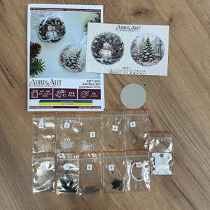 Peut inclure: Un kit de broderie de perles repr&eacute;sentant une sc&egrave;ne d'hiver avec un bonhomme de neige et un sapin de No&euml;l. Le kit comprend 10 couleurs de perles tch&egrave;ques Preciosa, une toile d'art naturelle et des instructions. Le kit mesure 24 pouces par 24 pouces (61 cm par 61 cm).