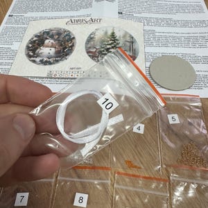 Peut inclure: Un gros plan d'un kit de bricolage pour une d&eacute;coration de No&euml;l. Le kit comprend un ruban blanc, des perles de diff&eacute;rentes couleurs et un rond de carton. Le kit est &eacute;tiquet&eacute; avec le num&eacute;ro 10.