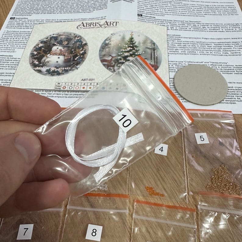 Peut inclure: Un gros plan d'un kit de bricolage pour une d&eacute;coration de No&euml;l. Le kit comprend un ruban blanc, des perles de diff&eacute;rentes couleurs et un rond de carton. Le kit est &eacute;tiquet&eacute; avec le num&eacute;ro 10.