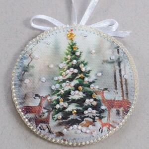 Peut inclure: Une boule de No&euml;l ronde en feutre avec un ruban blanc. La boule repr&eacute;sente une sc&egrave;ne de No&euml;l vintage avec un sapin vert d&eacute;cor&eacute; de perles blanches et dor&eacute;es, deux cerfs et un petit renard. La boule est entour&eacute;e d'une bordure de perles blanches.