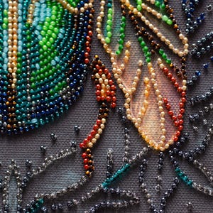Peut inclure: Gros plan sur une &oelig;uvre d'art en perles pr&eacute;sentant un motif color&eacute; avec des perles vertes, bleues et orange. Les perles sont dispos&eacute;es selon un motif qui ressemble &agrave; des plumes et des feuilles.