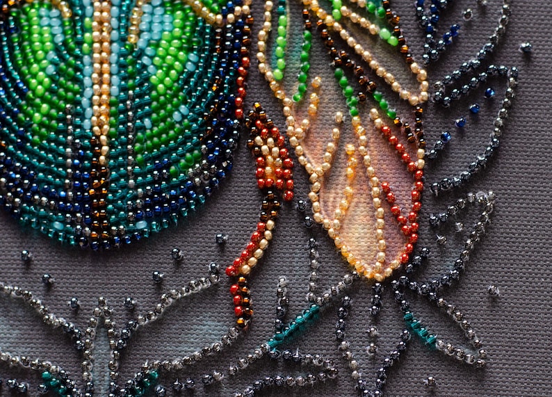 Peut inclure: Gros plan sur une &oelig;uvre d'art en perles pr&eacute;sentant un motif color&eacute; avec des perles vertes, bleues et orange. Les perles sont dispos&eacute;es selon un motif qui ressemble &agrave; des plumes et des feuilles.