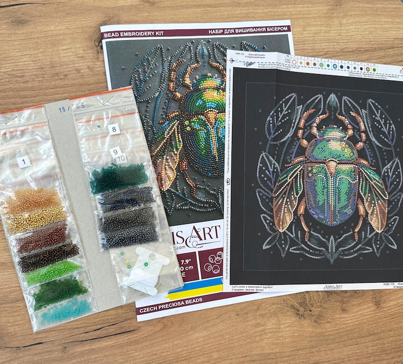Peut inclure: Un kit de broderie de perles repr&eacute;sentant un scarab&eacute;e vert et or aux d&eacute;tails complexes. Le kit comprend une toile noire, des perles de diff&eacute;rentes couleurs et des instructions. Le kit est &eacute;tiquet&eacute; "Bead Embroidery Kit" et "Набір для вишивання бісером".