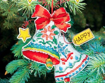 May include: Cross-stitched Christmas bell ornaments with a red bow and the word "HAPPY" on a yellow tag. The bells are white with colorful patterns and are hanging on a pine tree branch. Yellow star ornaments are also present.