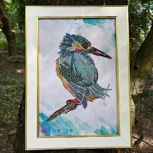 May include: A framed diamond painting of a blue and green kingfisher bird with a long beak, perched on a branch. The background is a watercolor-style wash of blue and purple.