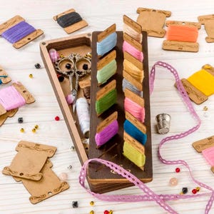 May include: Wooden box with a variety of colored threads and spools, a pair of scissors, and a thimble. The box is open and the threads are organized in a row.