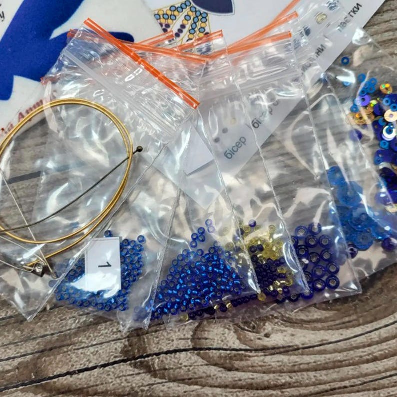 Puede incluir: Un conjunto de peque&ntilde;as bolsas de pl&aacute;stico que contienen cuentas azules y doradas, un alambre dorado y una etiqueta blanca con la palabra "Bicep" escrita en ella.