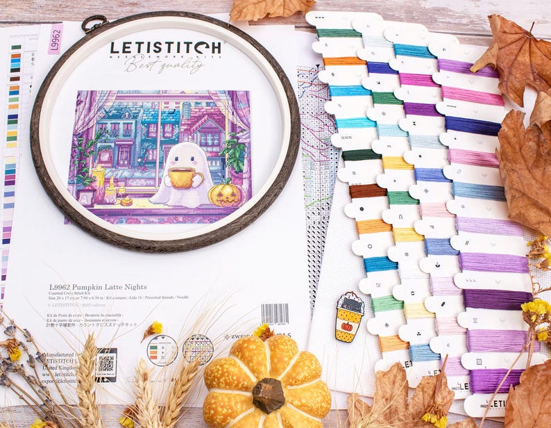 May include: A cross-stitch kit with a fall theme, featuring a ghost holding a coffee cup, a pumpkin, and a cityscape. The kit includes a wooden hoop, colorful embroidery floss, and a pattern. The text on the kit reads "LETISTITCH" and "Pumpkin Latte Nights".