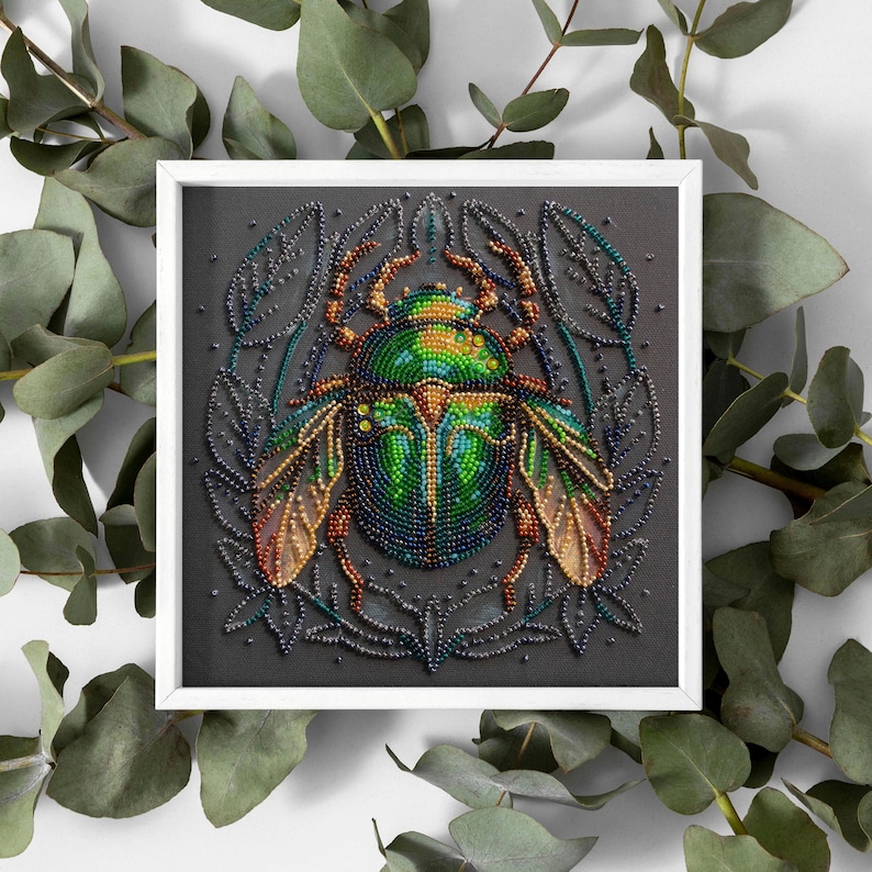 Peut inclure: Gros plan sur un scarab&eacute;e en perles vert et bleu aux ailes iris&eacute;es, sur fond noir avec un motif floral. Le scarab&eacute;e est une &oelig;uvre d'art en perles.