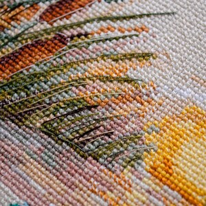 May include: Close-up of a cross-stitch embroidery with a detailed design of green leaves and yellow flowers. The fabric is white with a subtle texture.
