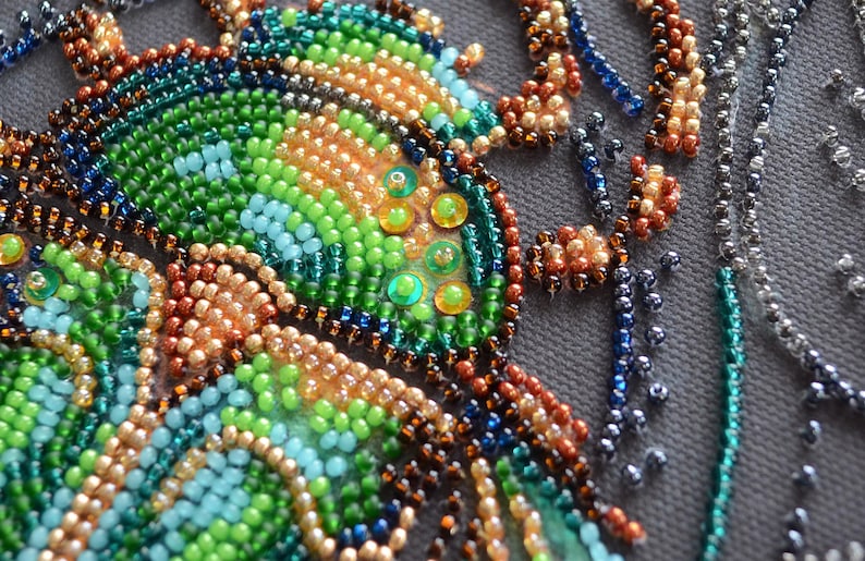 Peut inclure: Gros plan sur un motif de perles repr&eacute;sentant un papillon avec des perles vertes, bleues et brunes. Les perles sont dispos&eacute;es en un motif qui ressemble aux ailes d'un papillon.
