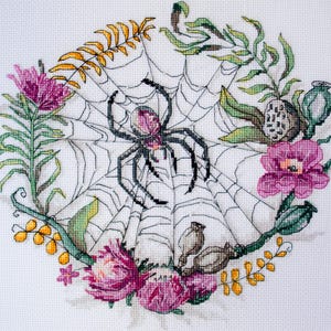Könnte beinhalten: Ein Kreuzstich-Stickmuster mit einer schwarzen Spinne in einem Netz, umgeben von rosa und gelben Blumen und grünen Blättern.