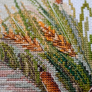 May include: Close-up of a cross-stitch embroidery featuring a detailed design of green and brown grass with orange accents.