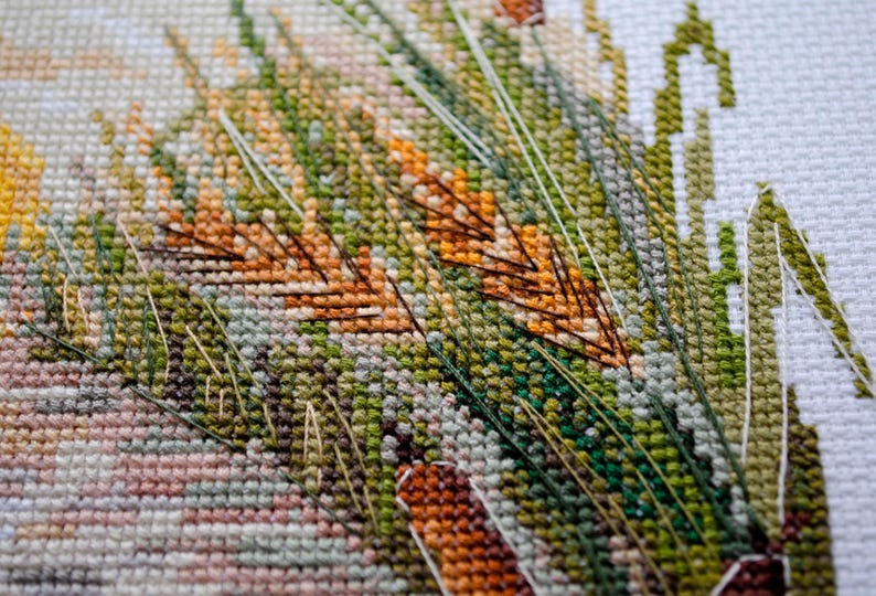 May include: Close-up of a cross-stitch embroidery featuring a detailed design of green and brown grass with orange accents.