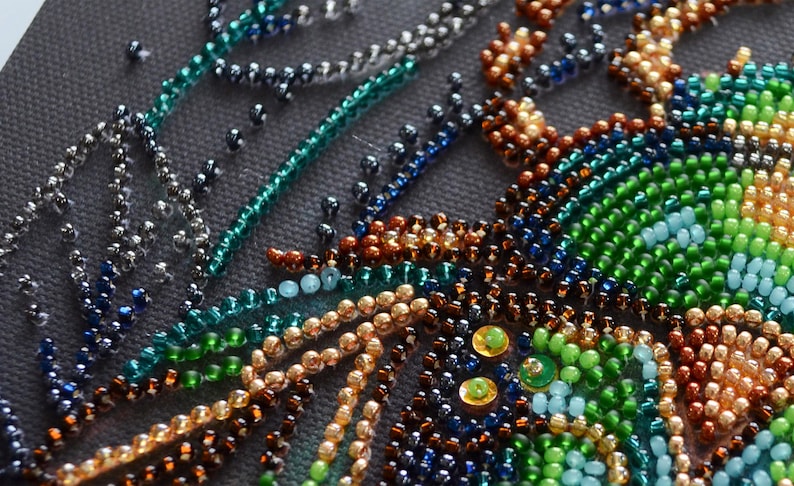 Peut inclure: Gros plan sur une &oelig;uvre d'art en perles avec un motif tourbillonnant de perles vertes, bleues, brunes et dor&eacute;es.