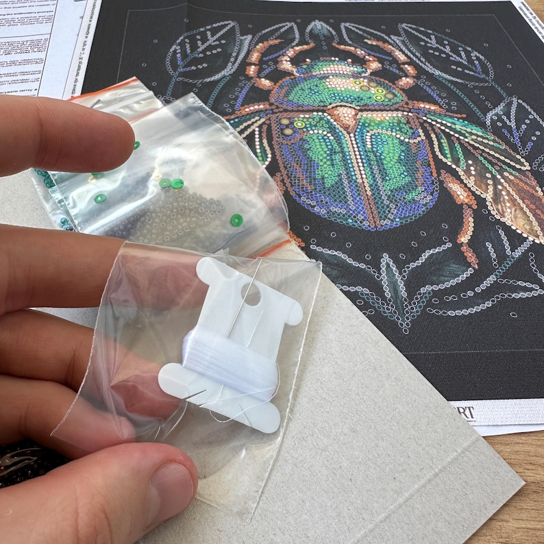 Peut inclure: Un kit de peinture diamant de pr&egrave;s, mettant en sc&egrave;ne un scarab&eacute;e vert et bleu aux d&eacute;tails complexes. Le kit comprend une toile, des perles, un enfileur et un sac de perles.