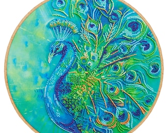 Könnte beinhalten: Ein runder Stickrahmen mit einem Perlen-Pfauen-Design. Der Pfau ist blau, grün und gold mit einem detaillierten Federmuster. Der Hintergrund ist ein hellblauer und grüner Aquarell-Wasch.