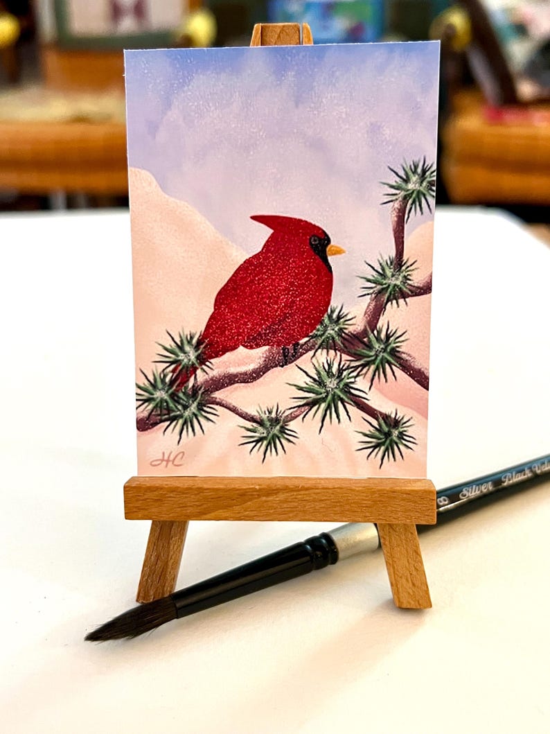 May include: A watercolour painting of a red cardinal perched on a branch of a snow-covered tree. The background is a light blue sky with white snow falling. The painting is signed "HC" in the bottom left corner.