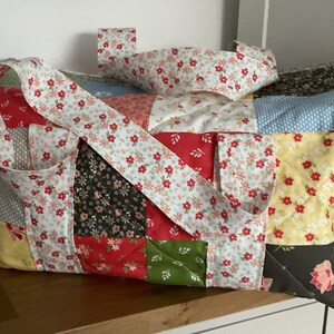 May include: A patchwork tote bag with a floral print. The bag has a large, rectangular shape and is made of different colored fabrics. The bag has a long strap that can be worn over the shoulder.