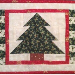 Könnte beinhalten: Ein weißer gesteppter Platzdeckchen mit rotem Rand und einem grünen Weihnachtsbaumdesign. Der Baum ist aus Stoff mit einem Stechpalmenmuster und hat einen braunen Stamm.