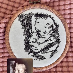 May include: Embroidered artwork in a wooden hoop featuring a black and white sketch of a baby. A small ultrasound image is placed below the embroidery. The background is a pink, textured fabric.