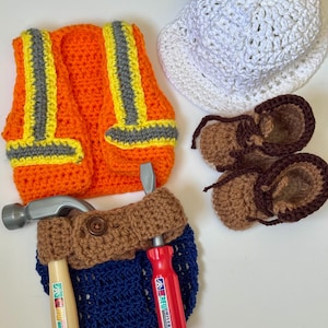 May include: A crochet construction worker set in orange, yellow, gray, white, brown, and blue. The set includes a vest, hat, boots, and tool belt with toy tools. The vest has reflective stripes. The boots have brown laces.