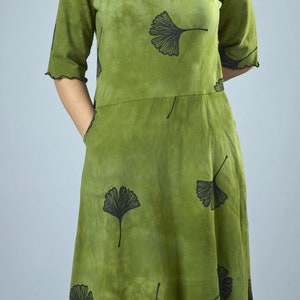 May include: A green dress with a black ginkgo leaf print. The dress has a round neckline and 3/4 sleeves. The dress has a ruffled hem.