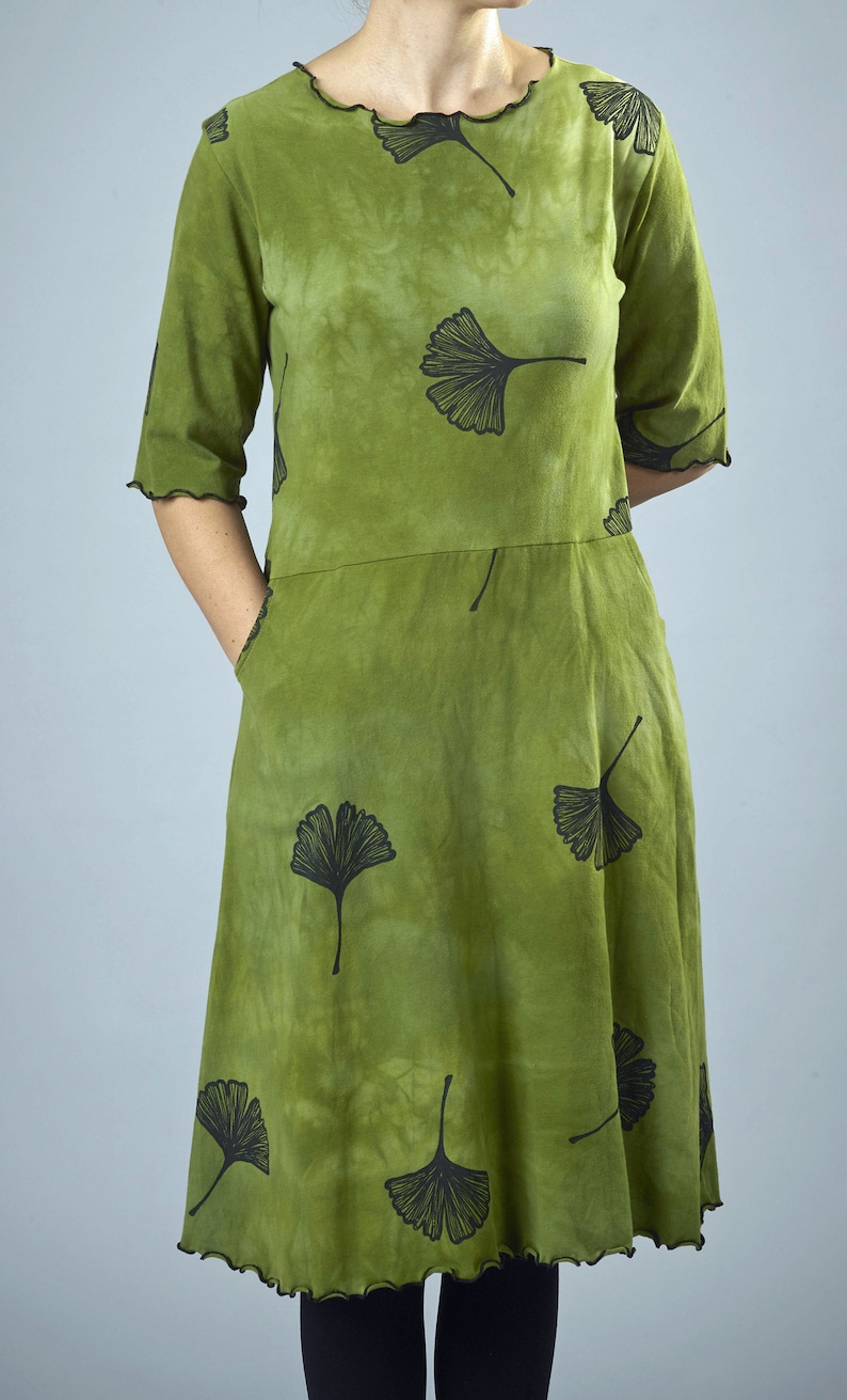 May include: A green dress with a black ginkgo leaf print. The dress has a round neckline and 3/4 sleeves. The dress has a ruffled hem.