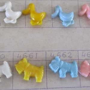 Puede incluir: Un conjunto de diez botones de plástico con forma de patos y perros. Los patos son blancos, amarillos, azules y rosas. Los perros son blancos, amarillos, azules y rosas. Los botones están numerados del 4660 al 4663.