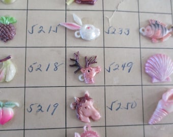 May include: A collection of plastic charms with various designs, including a pineapple, a banana, a peach, a rabbit, a deer, a horse, a seashell, and a conch shell. Each charm has a small hole for attaching to a necklace or bracelet. The charms are arranged on a grid with numbers written next to them.