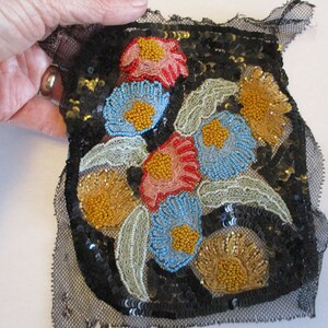May include: A black mesh fabric with a floral design embroidered with sequins and beads. The flowers are in shades of blue, red, yellow, and gold.