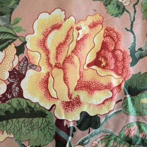 May include: A pink fabric with a floral pattern featuring yellow, red, and green roses. The fabric has a vintage aesthetic.