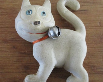 May include: White ceramic cat figurine with blue eyes and an orange collar with a silver bell. The cat is smiling and has a playful expression.