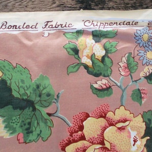 May include: A pink fabric with a floral pattern featuring green leaves, yellow and pink flowers, and blue flowers. The fabric has a label that reads "A Boncled Fabric 'Chippendale'  the  eye"