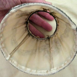 May include: A white fabric lampshade with a black trim and a metal ring inside. The lampshade is made of a soft, delicate material.