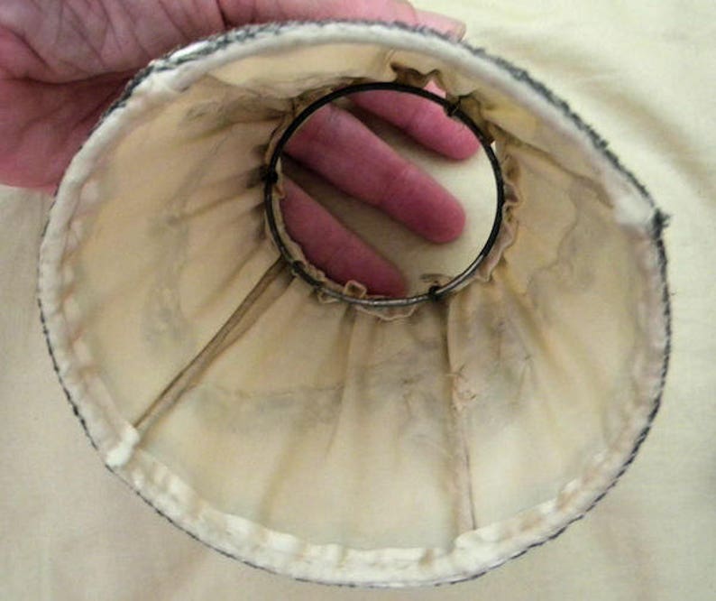 May include: A white fabric lampshade with a black trim and a metal ring inside. The lampshade is made of a soft, delicate material.