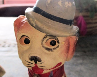May include: A white ceramic dog figurine wearing a blue and black hat and a red scarf. The dog has black eyes and a painted black nose.